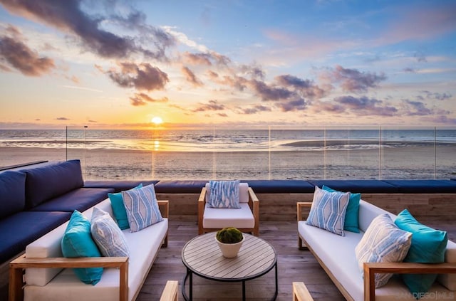 deck at dusk with a water view, outdoor lounge area, and a beach view