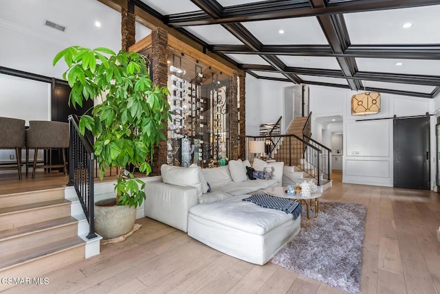 living room with coffered ceiling, crown molding, beamed ceiling, a barn door, and light hardwood / wood-style floors