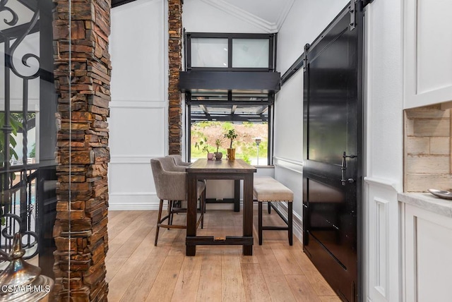 dining space featuring ornamental molding, a barn door, lofted ceiling, and light hardwood / wood-style floors