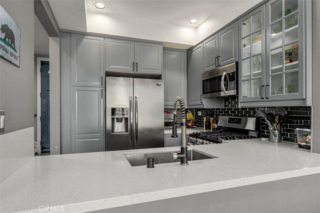 kitchen featuring stainless steel appliances, light stone countertops, decorative backsplash, and gray cabinetry