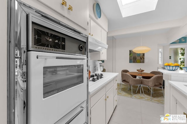 kitchen featuring light tile patterned flooring, white cabinets, white appliances, and a skylight