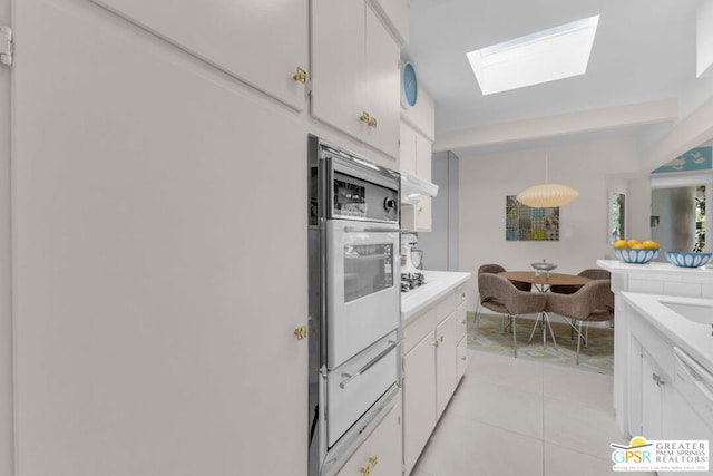 kitchen with white cabinetry, a skylight, hanging light fixtures, light tile patterned floors, and white appliances