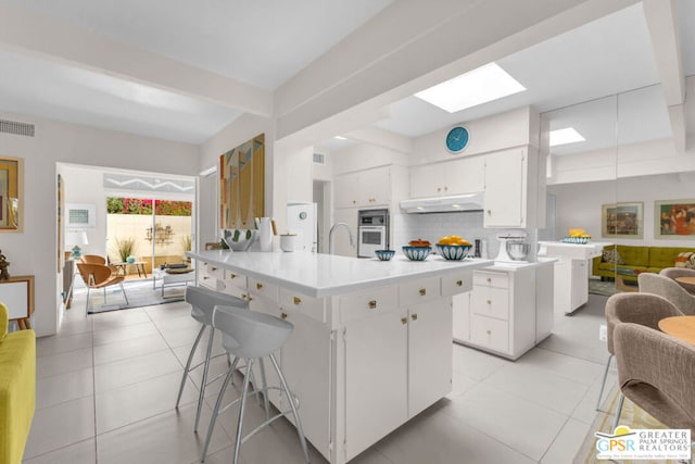 kitchen featuring a skylight, an island with sink, sink, white cabinets, and decorative backsplash