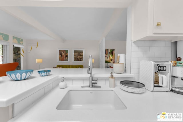 interior details with sink, white cabinets, decorative backsplash, kitchen peninsula, and beamed ceiling