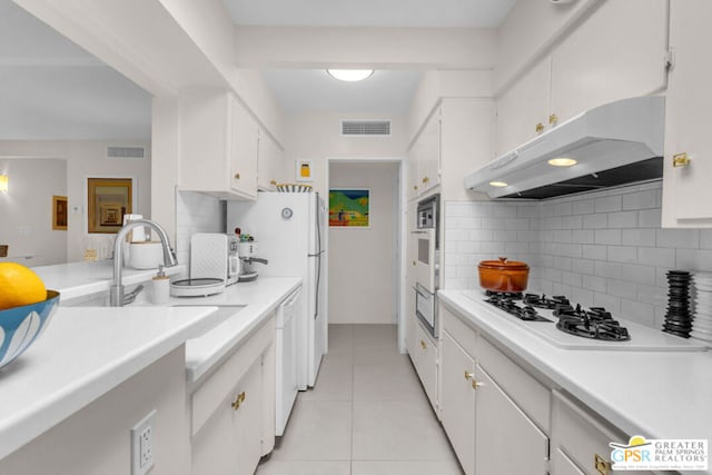 kitchen with sink, white appliances, light tile patterned floors, white cabinetry, and backsplash