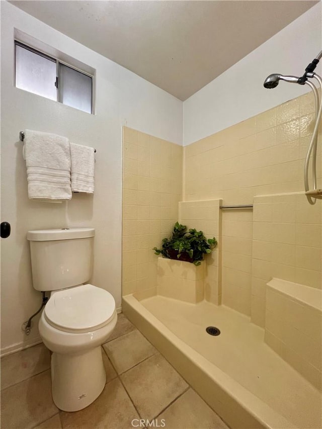 bathroom with toilet, tile patterned flooring, and a tile shower