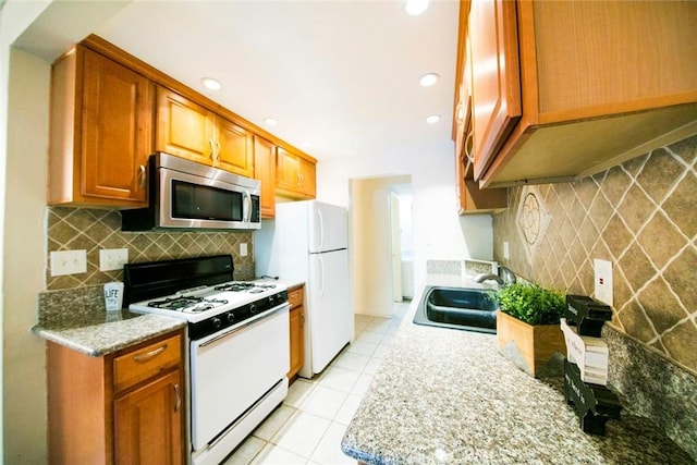 kitchen featuring tasteful backsplash, white appliances, light stone countertops, and sink