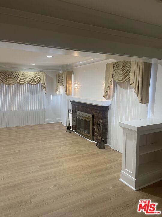 basement featuring light hardwood / wood-style floors and a brick fireplace