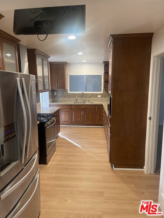 kitchen featuring sink, light hardwood / wood-style flooring, appliances with stainless steel finishes, range hood, and tasteful backsplash