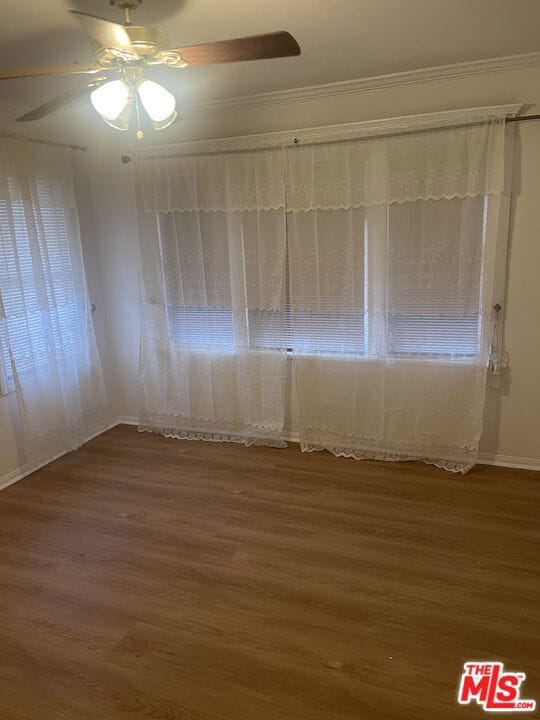 empty room with crown molding, dark wood-type flooring, and ceiling fan