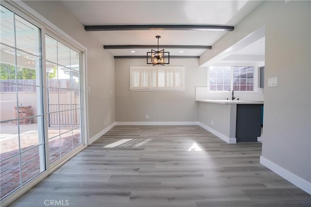 unfurnished dining area featuring beamed ceiling, a chandelier, sink, and hardwood / wood-style flooring