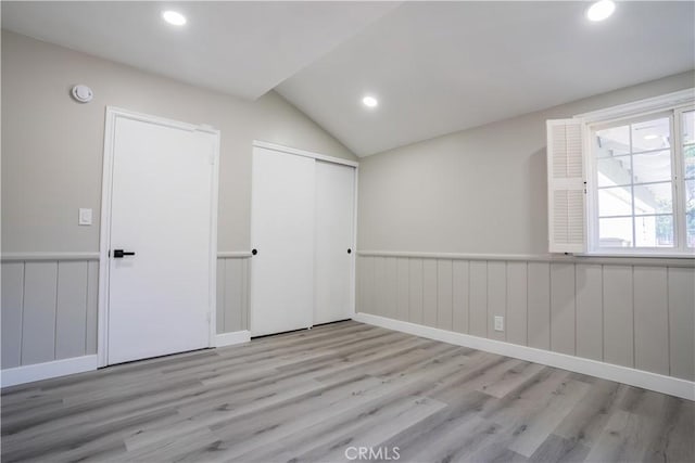 unfurnished bedroom featuring vaulted ceiling, a closet, and light wood-type flooring