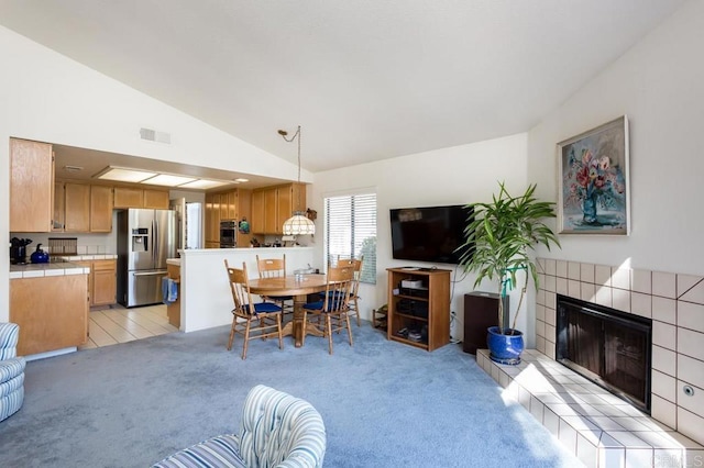 dining room with lofted ceiling, a tiled fireplace, and light colored carpet