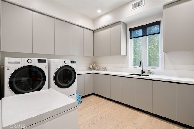 washroom with cabinets, washing machine and dryer, sink, and light hardwood / wood-style floors