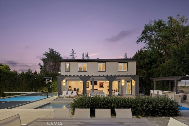 back house at dusk with an outdoor living space, a pergola, and tennis court