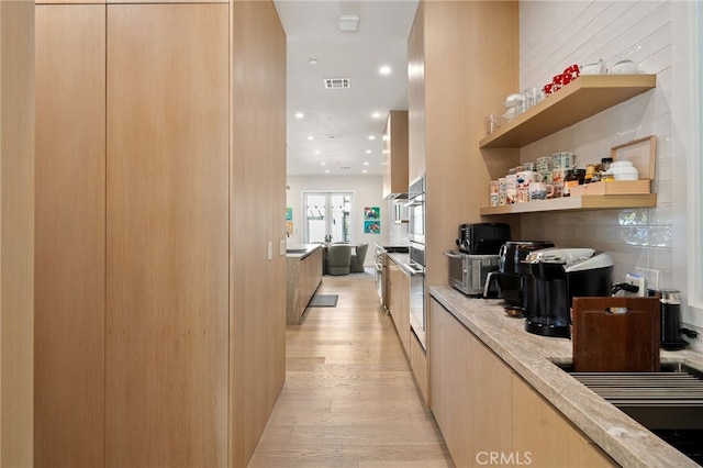 bar featuring light brown cabinetry, oven, decorative backsplash, and light wood-type flooring