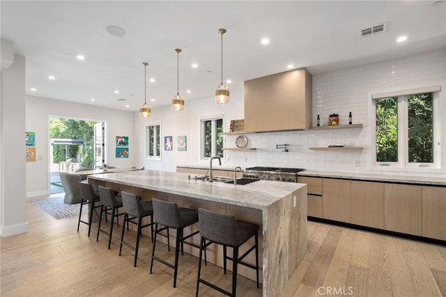 kitchen featuring pendant lighting, a large island, light stone countertops, light hardwood / wood-style floors, and wall chimney range hood