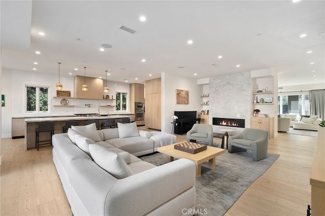 living room featuring a high end fireplace, light hardwood / wood-style flooring, and a wealth of natural light