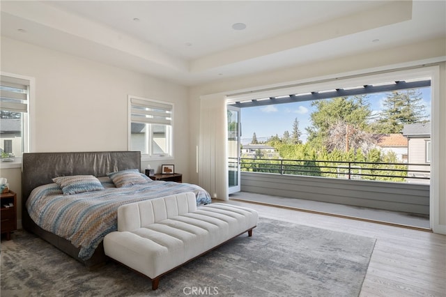 bedroom featuring hardwood / wood-style flooring, a tray ceiling, and access to outside