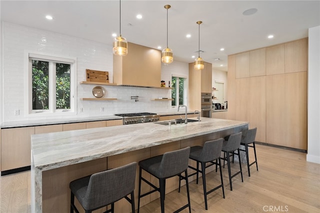 kitchen featuring sink, stove, hanging light fixtures, light stone countertops, and a large island with sink