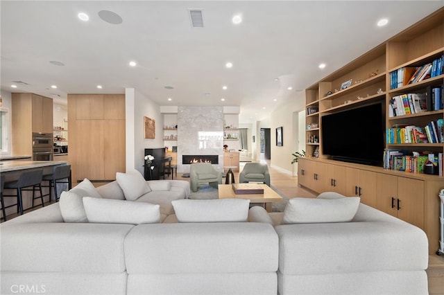 living room featuring built in shelves, light hardwood / wood-style floors, and a large fireplace