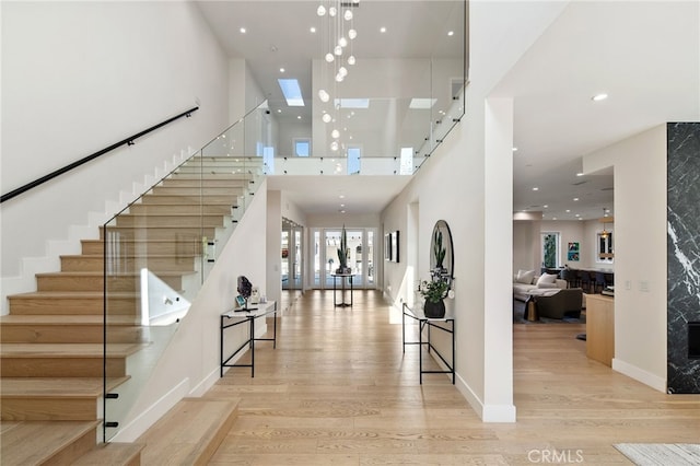 foyer entrance with a towering ceiling, a skylight, and light wood-type flooring