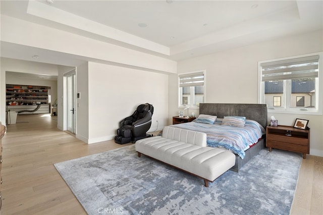 bedroom featuring a raised ceiling, light hardwood / wood-style floors, and multiple windows