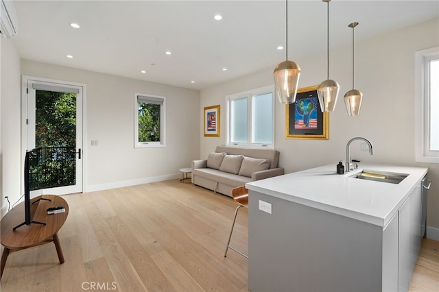 kitchen with pendant lighting, sink, light hardwood / wood-style floors, kitchen peninsula, and a healthy amount of sunlight