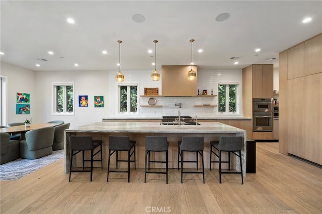 kitchen featuring a kitchen bar, hanging light fixtures, a large island, light stone counters, and light hardwood / wood-style floors