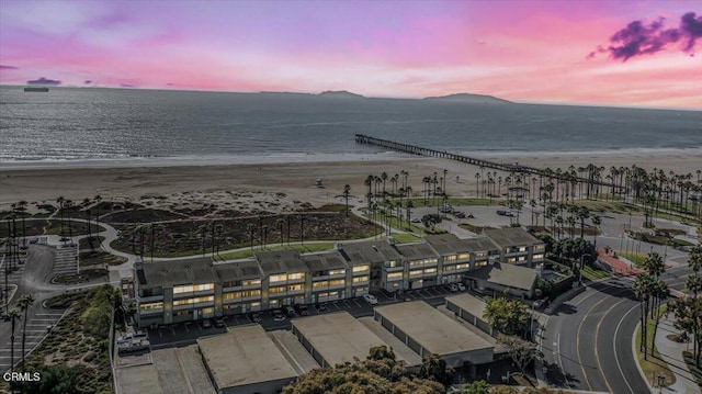 aerial view at dusk featuring a view of the beach and a water view