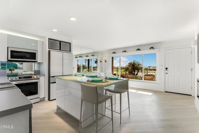 kitchen featuring stainless steel electric stove, fridge, white cabinets, and light hardwood / wood-style flooring