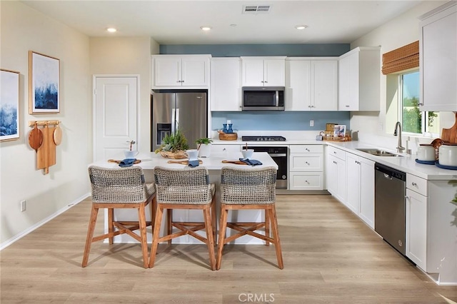 kitchen with sink, white cabinetry, stainless steel appliances, a center island, and a kitchen bar