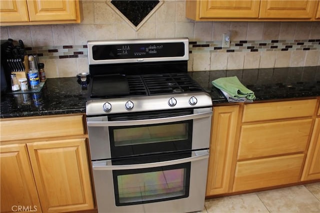 kitchen featuring tasteful backsplash, double oven range, dark stone counters, and light tile patterned flooring