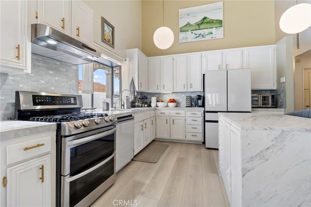 kitchen with stainless steel appliances, a towering ceiling, pendant lighting, and white cabinets