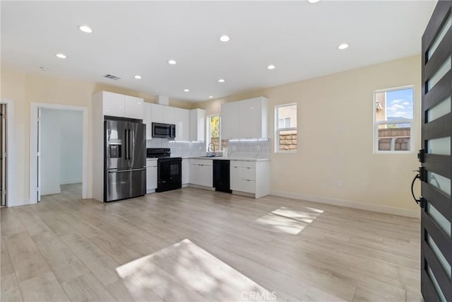 kitchen with tasteful backsplash, white cabinetry, a healthy amount of sunlight, and black appliances