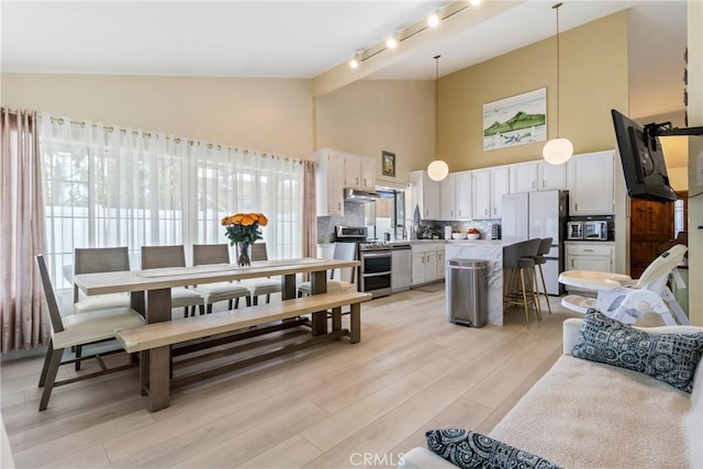 interior space featuring a breakfast bar area, white cabinetry, stainless steel appliances, tasteful backsplash, and decorative light fixtures