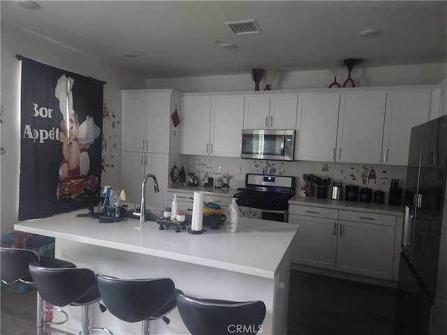 kitchen with stainless steel appliances, an island with sink, and white cabinets