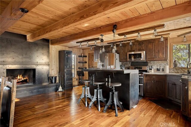 kitchen with decorative light fixtures, dark brown cabinets, a kitchen breakfast bar, a kitchen island, and stainless steel appliances