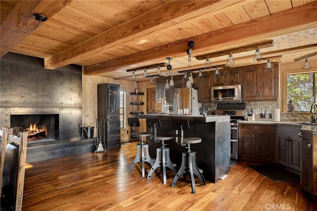 kitchen with a kitchen bar, a center island, hanging light fixtures, dark brown cabinets, and stainless steel appliances