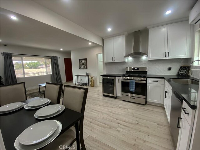 kitchen with tasteful backsplash, appliances with stainless steel finishes, wall chimney range hood, beverage cooler, and white cabinets