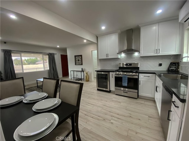 kitchen featuring dark countertops, appliances with stainless steel finishes, white cabinets, wall chimney range hood, and beverage cooler