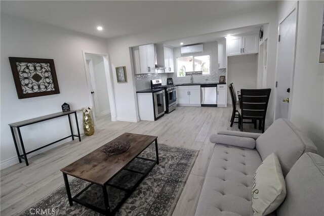 living room featuring sink, a wall unit AC, and light wood-type flooring