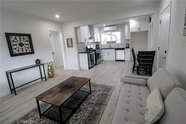 living room featuring sink, a wall mounted AC, and light hardwood / wood-style flooring