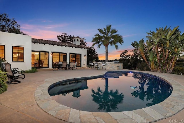 pool at dusk featuring a patio