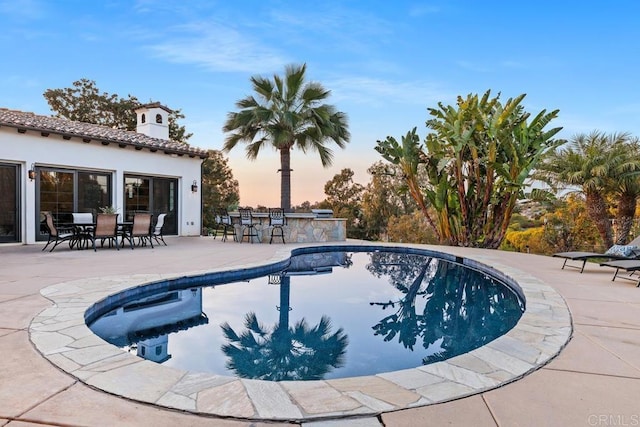 pool at dusk with a patio and a bar