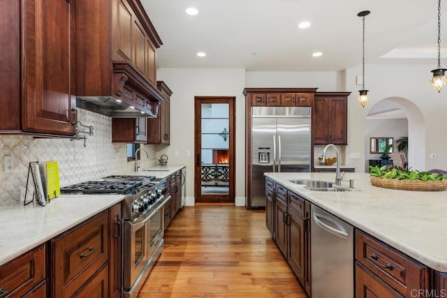 kitchen featuring pendant lighting, high quality appliances, sink, and light hardwood / wood-style flooring