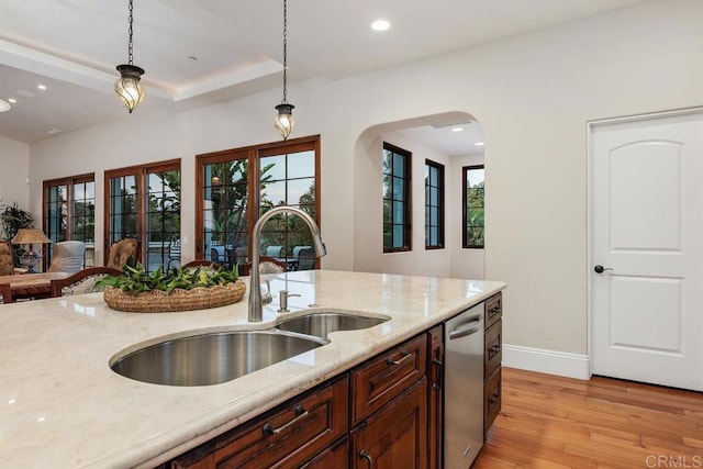 kitchen featuring sink, light hardwood / wood-style flooring, light stone counters, decorative light fixtures, and a raised ceiling