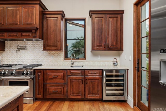 kitchen with sink, tasteful backsplash, light hardwood / wood-style flooring, appliances with stainless steel finishes, and beverage cooler