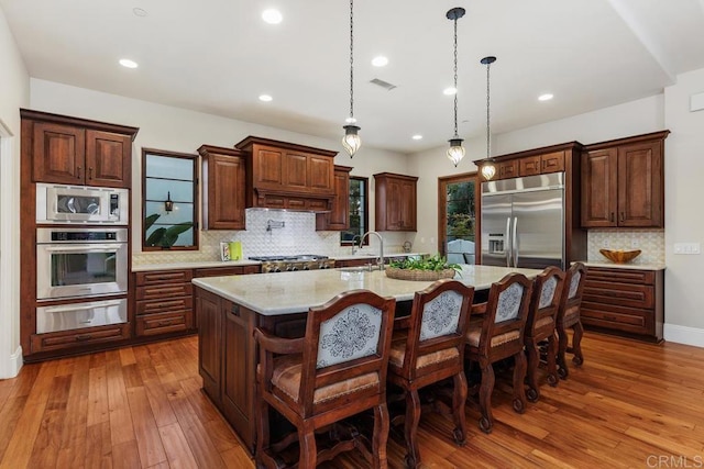 kitchen featuring a large island, sink, built in appliances, a kitchen bar, and decorative light fixtures