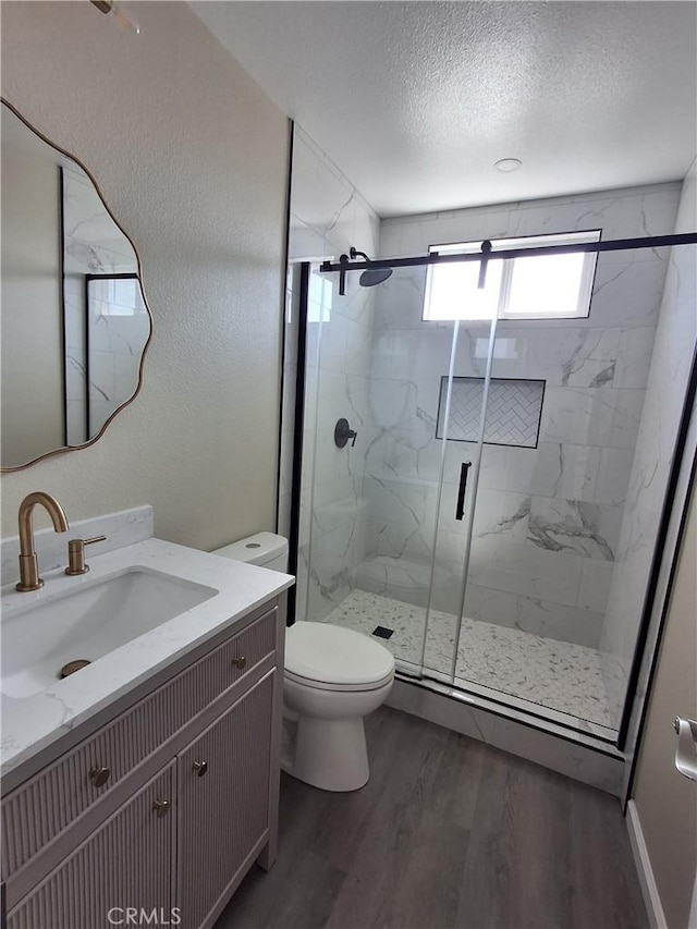 bathroom with a shower with door, vanity, wood-type flooring, a textured ceiling, and toilet